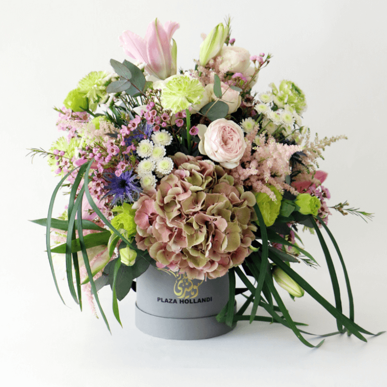 Loose flower arrangement in a Plaza Hollandi Hat box ranunculus, hydrangea, wax flower, eryngium, astilbe, lily arrangement in a Plaza Hollandi Hat Box