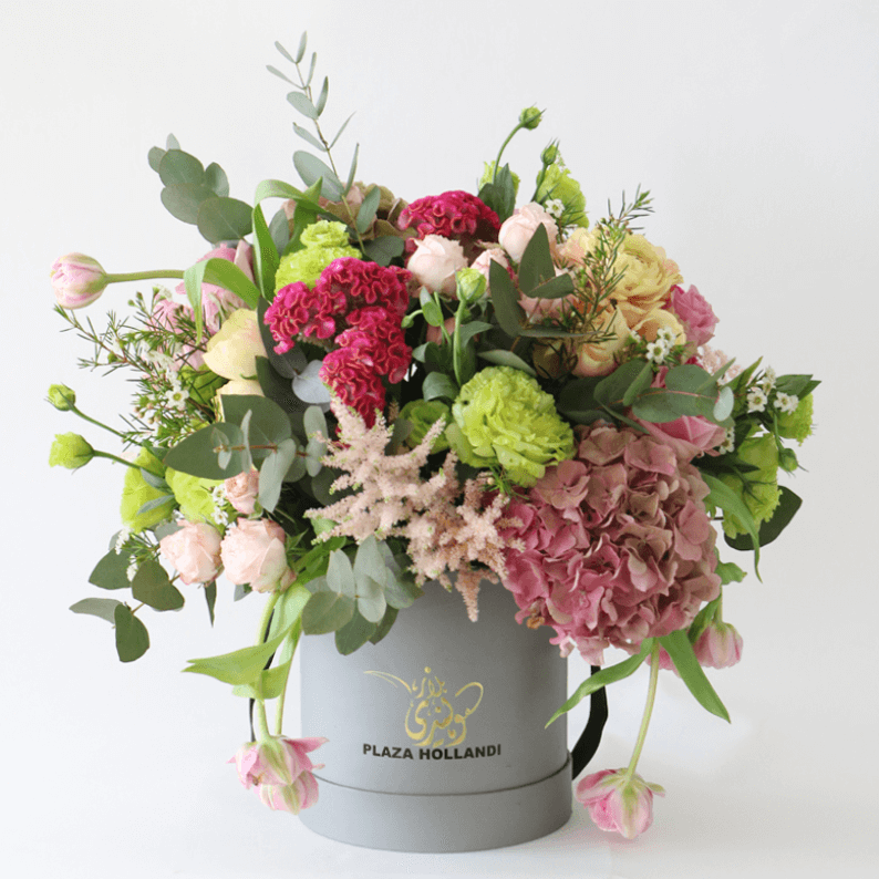 a loose european arrangement in a hat box pink, green and peach flowers arranged in a hat box